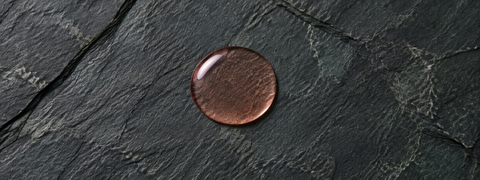 A single translucent pink-amber drop of N°00 on cold slate.